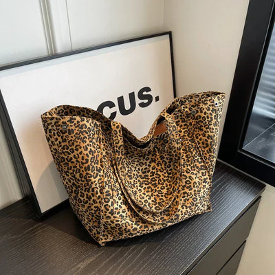 Sac à main imprimé léopard sur une table noire, devant un cadre avec le mot "CUS." Design élégant, tendance mode, accessoire féminin chic.