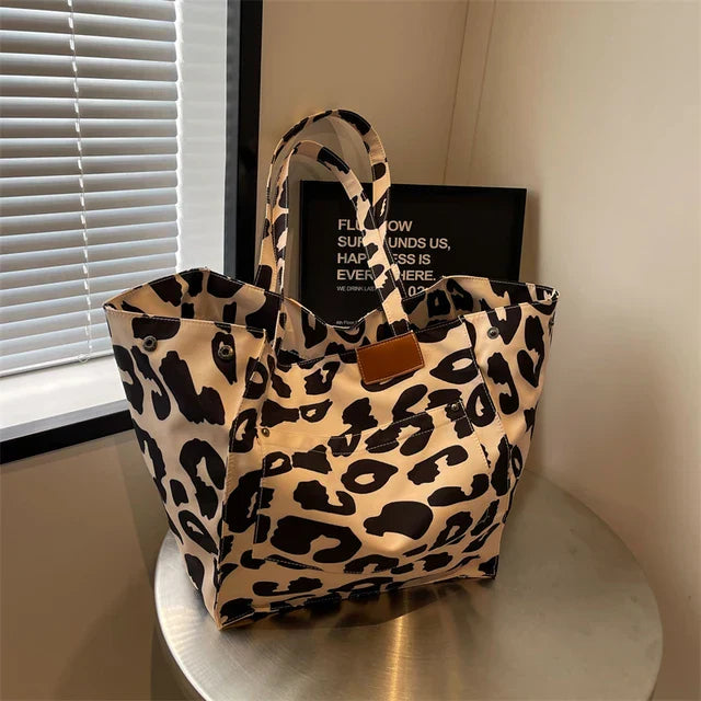 Sac à main en toile imprimé léopard sur une table, près d'une fenêtre avec stores. Accessoire mode tendance, design animalier chic et moderne.
