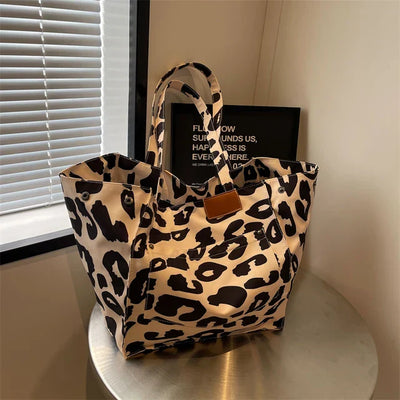 Sac à main en toile imprimé léopard sur une table, près d'une fenêtre avec stores. Accessoire mode tendance, design animalier chic et moderne.