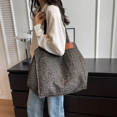Femme portant un grand sac à main léopard, chemise blanche et jean, debout près d'une commode noire. Mode tendance, accessoire animalier.