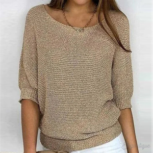 Femme portant un pull beige en maille, manches trois-quarts, col rond, avec un collier doré, sur fond blanc. Mode féminine élégante et décontractée.