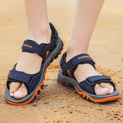 Sandales de randonnée bleues et orange sur plage, semelles antidérapantes, confortables, idéales pour activités extérieures, pieds nus visibles.