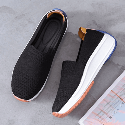 Chaussures de sport noires en maille respirante avec semelle blanche et détails colorés, posées sur un sol gris. Confort et style moderne.