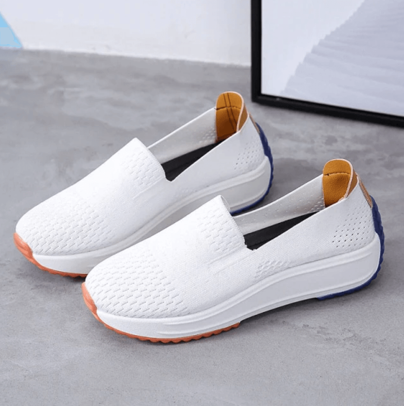 Chaussures blanches en toile, semelles épaisses, détails orange et bleu, design moderne et confortable, posées sur un sol gris.