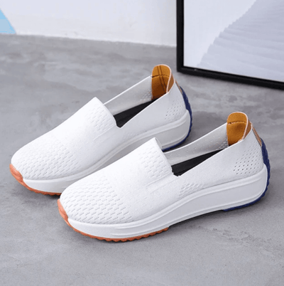 Chaussures blanches en toile, semelles épaisses, détails orange et bleu, design moderne et confortable, posées sur un sol gris.