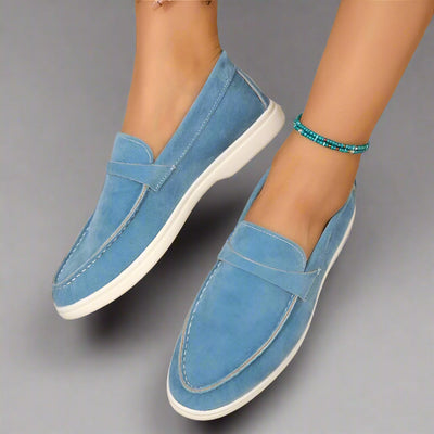 Chaussures mocassins bleu clair en daim pour femme, semelle blanche, portées avec un bracelet de cheville turquoise. Mode féminine élégante.